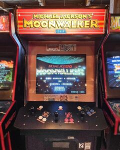 Máquina recreativa arcade de Michael Jackson's Moonwalker con la pantalla encendida mostrando el título del juego y el logo de SEGA.