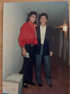 Michael Jackson posa de pie junto a un seguidor en un pasillo interior.