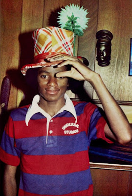 Michael Jackson sonriendo mientras sostiene un sombrero de copa de colores con una flor encima.