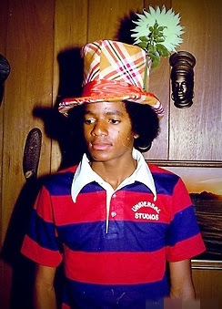 Michael Jackson vistiendo una camisa de rayas rojas y azules de Universal Studios y un sombrero de copa con estampado de cuadros y una flor.