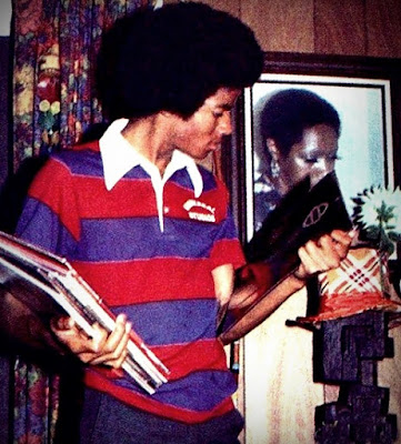 Michael Jackson joven con peinado afro, vistiendo una camisa de rayas rojas y azules, sosteniendo varios discos de vinilo en sus manos.